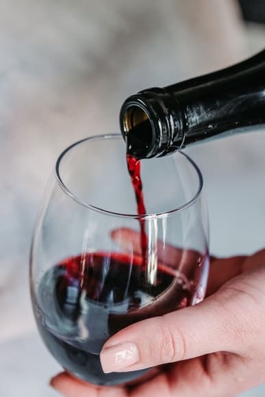 A glass of red wine being poured from a bottle.